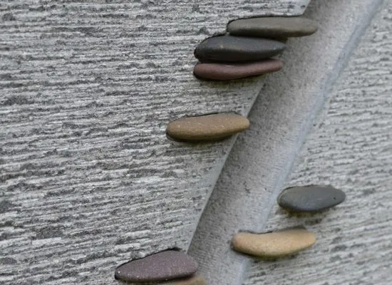Gestockte Steinfläche mit geschwungener Linie und eingelegten farbigen Kieseln