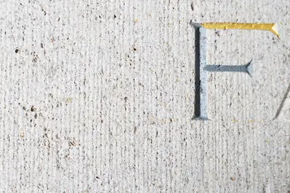 In hellen Stein gehauener Buchstabe F, der obere Balken golden gefasst